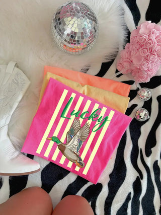 Neon pink striped tee with flying mallard duck graphic and green "Lucky" script lettering.