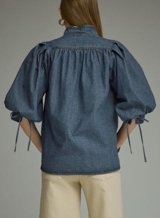 Medium wash denim top with voluminous puff sleeves, gathered yoke back, and tie cuff details.