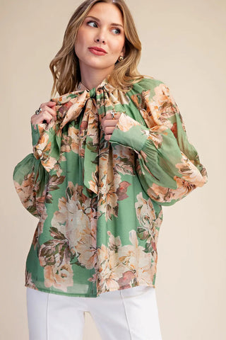 Green floral print chiffon blouse with tie-neck bow detail and billowy long sleeves, worn with white pants.