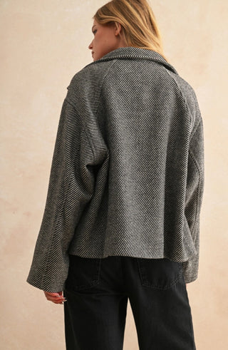 Oversized herringbone black and white cape-style jacket with wide sleeves, worn over black pants, back view.