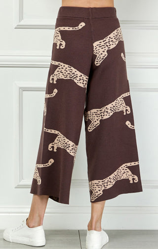 Dark brown wide-leg cropped knit pants featuring repeated beige leaping leopard print pattern, styled with white sneakers.