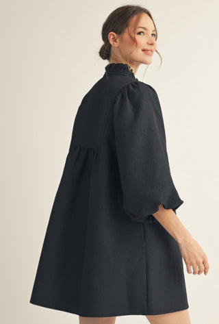 Black babydoll mini dress with 3/4 balloon sleeves, ruffled mock neckline, and relaxed A-line silhouette.