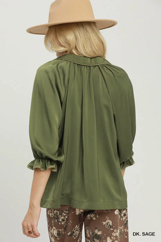 Dark sage green collared blouse with gathered back, puff sleeves, and ruffle cuffs, worn with floral pants.