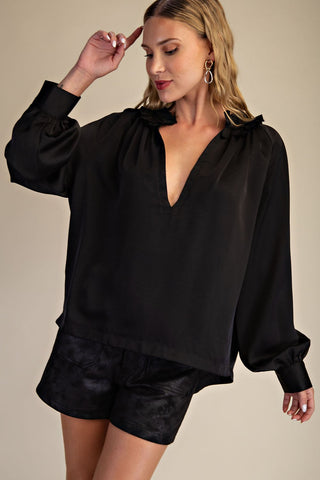 Black satin V-neck blouse with ruffled neckline, balloon sleeves, and structured cuffs paired with black shorts.
