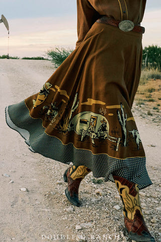 Brown western swing skirt with cowboy camp scene border print, gingham ruffle hem, worn with decorative cowboy boots.