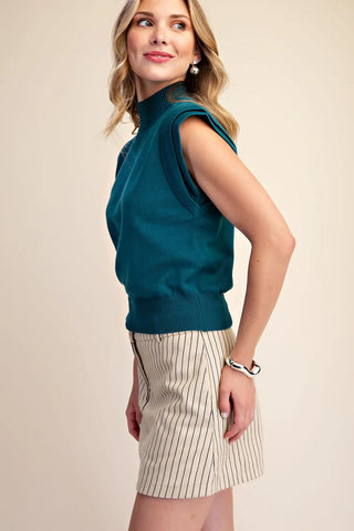 Teal high neck sleeveless fine knit sweater top with structured shoulders, worn with pinstripe mini skirt.