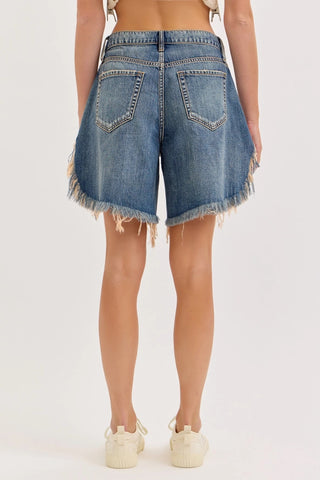 Woman wearing mid-rise blue denim cutoff shorts with frayed hem and faded wash, back view.