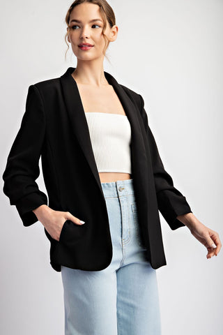 Black shawl lapel open-front blazer with ruched sleeves and side pockets, styled casually.