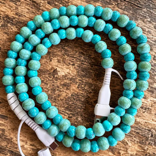 Turquoise howlite beaded 4-in-1 charging cable coiled on rustic wood surface with white USB connectors visible.