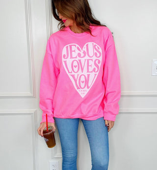 Neon pink crewneck sweatshirt with "Jesus Loves You" heart graphic, styled with blue jeans.