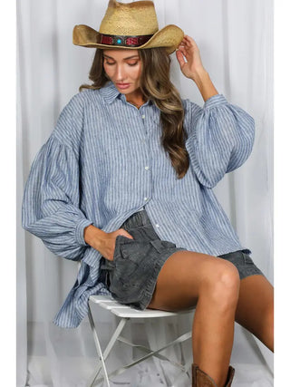 Oversized blue and white striped button-up shirt with dramatic balloon sleeves, paired with denim shorts and cowboy hat.