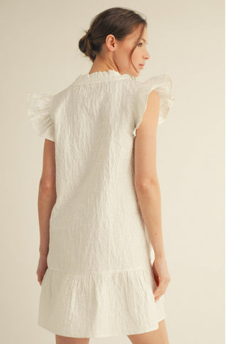 White textured mini dress with ruffled cap sleeves, ruffle hem, and scalloped neckline detail.
