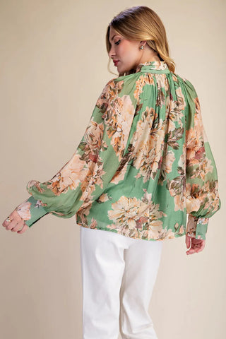 Green floral print tie-neck blouse with balloon sleeves and button cuffs, paired with white pants.