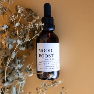 Amber glass dropper bottle of Evergreen Apothecary Mood Boost Saffron Tincture, made in Utah, beside dried wildflowers.