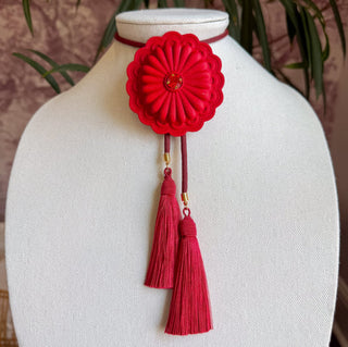 Red flower concho bolo tie necklace with crimson pendant, gold accents, and dual maroon tassels on leather cord.