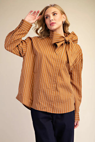 Camel brown pinstripe high neck shirt with oversized bow detail and buttoned cuffs, paired with navy trousers.