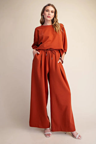 Rust orange wide-leg sweatpants with elastic waistband, drawstring tie, and side pockets, styled with matching top.