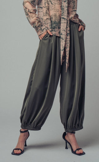 Olive green satin relaxed fit boho pants with gathered elastic ankles, worn with black strappy heels.