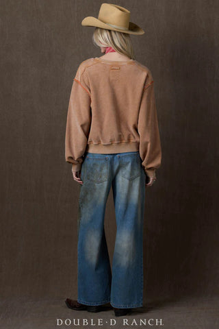 Camel-toned acid-washed sweatshirt with contrast orange seams, worn with wide-leg jeans and cowboy hat.