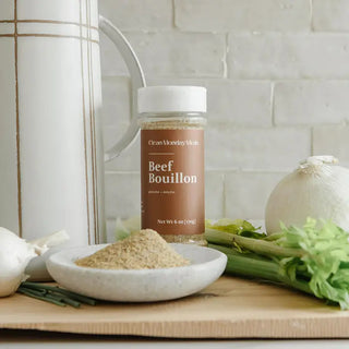 Clean Monday Meats Beef Bouillon powder jar with bouillon displayed in small marble dish, surrounded by fresh celery, onions,