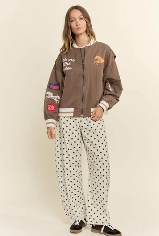 Brown zip-up bomber jacket with rodeo horse embroidery and patches, worn over polka dot pants.