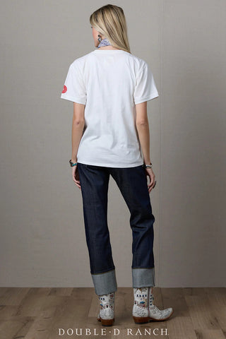 White short-sleeve graphic tee with red sleeve patch, worn with dark indigo cuffed jeans and embroidered western boots.