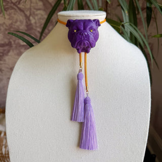 Purple bulldog head bolo tie with golden yellow cord and hanging lavender tassel accents on display bust.