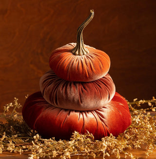 Three stacked velvet pumpkins in rust, bronze, and red with a natural stem, surrounded by dried florals.