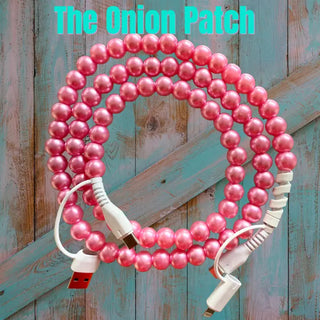 Pink iridescent pearl beaded charging cable coiled on rustic teal wood background, USB and Lightning connectors visible.