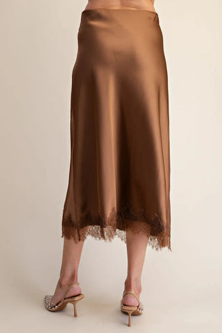 Brown satin midi skirt with delicate lace trim hem, worn with nude embellished heels, back view.