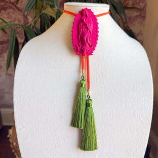 Hot pink Our Lady of Guadalupe bolo tie pendant with orange cord and two olive green silk tassels.