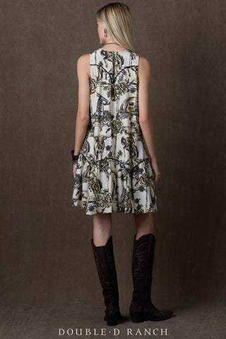 White sleeveless tunic dress with black and gold Western toile print, worn with dark brown cowboy boots.