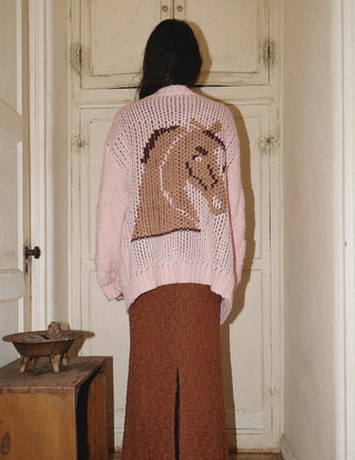 Pink open-knit cardigan with brown intarsia horse graphic on back, paired with rust wide-leg trousers.