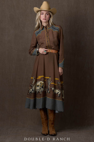 Brown western shirt dress with cowboy scene border print, checkered trim, yellow piping, and leather belt.