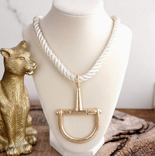 White twisted rope necklace with large gold horse bit pendant displayed on cream jewelry bust.