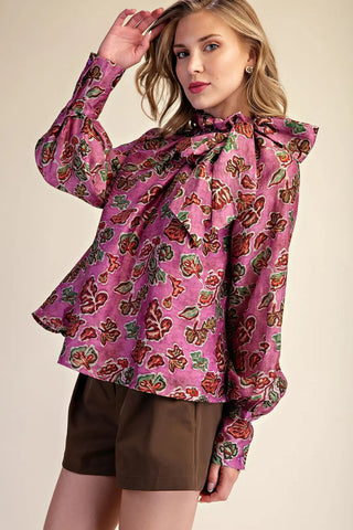 Purple floral print ruffle neck blouse with bow tie detail and long sleeves, paired with brown shorts.