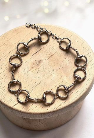 Silver chain link belt featuring snaffle bit equestrian details displayed on a round wooden jewelry box.