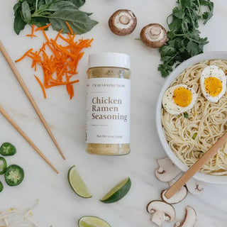 Beef Ramen Seasoning jar by Clean Monday Meals surrounded by fresh mushrooms, shredded carrots, lime wedges, and a noodle bow