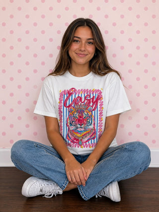 White graphic tee featuring colorful tiger illustration with "Easy" script text, worn by model seated cross-legged.