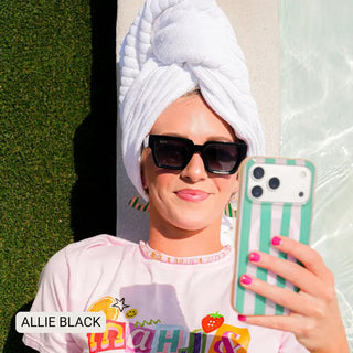 Woman wearing black polarized rectangle sunglasses with white hair towel wrap, taking poolside selfie.