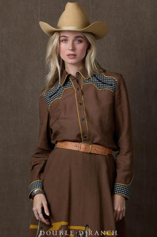 Brown western shirt with checkered yoke panels, gold piping trim, and snap buttons, styled with cowboy hat.