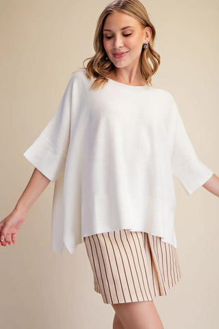 White oversized pullover sweater with short sleeves, relaxed fit, and ribbed hem detail.
