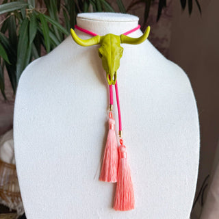 Olive green longhorn skull bolo tie necklace with fuchsia cord and peach tassel pendants displayed on white bust.