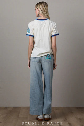 White short-sleeve baseball-style tee with blue trim, embroidered patch detail on sleeve, worn with wide-leg striped pants.