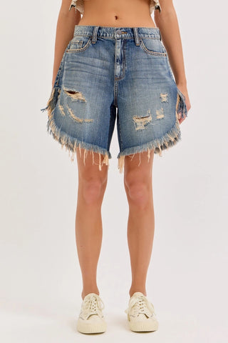 Mid waisted distressed blue denim cut off shorts with frayed hem and ripped details, styled with white sneakers.