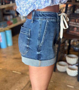High-waist medium wash denim cuff jogger shorts with patch pocket, rolled hem, and tie waistband detail.