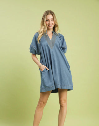 Oversized blue denim mini dress with puff sleeves, V-neckline, and front pocket on model.