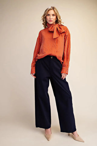 Orange and white striped long-sleeve shirt with high neck bow tie detail, styled with navy wide-leg trousers.