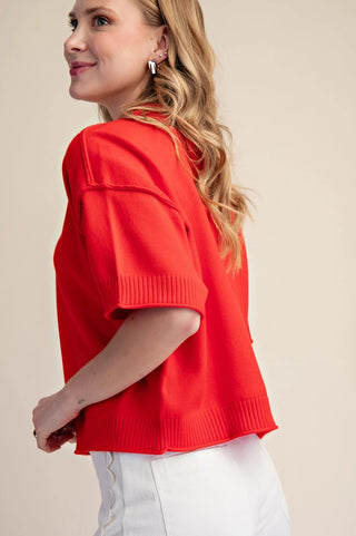 Red elbow-length sleeve cropped sweater with ribbed cuffs and hem seam detail, styled with white pants.