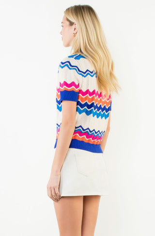 Short sleeve cream knit top with colorful blue, pink, and orange zigzag stripe pattern, paired with white mini skirt.